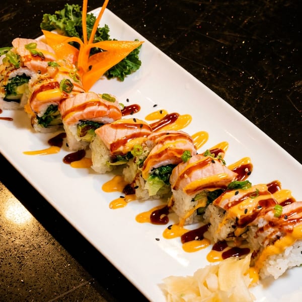 A long white plate of sushi rolls topped with salmon, sauces, and sesame seeds.